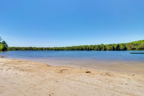 Ein sandiger Strand mit einem ruhigen See und einer bewaldeten Hügelkette im Hintergrund.
