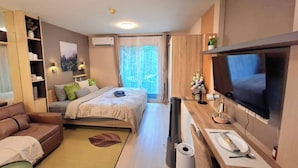 A modern hotel room with a bed, a sofa, a TV, a desk, and a large window. - Modern Studio Pool View, King bed, BTS Punnawithi (Bangkok)