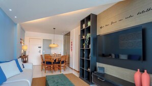 Ein modernes Wohnzimmer mit einer Couch, einem Esstisch, Stühlen, einem Fernseher und einem Bücherregal.