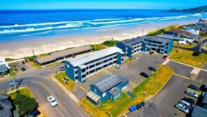 An aerial view of a coastal building complex with parking, a beach, and ocean views.