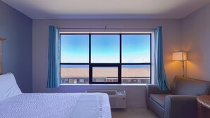 A hotel room with a large window, a bed, a chair, and a lamp.