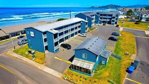 A coastal hotel with a parking lot, a building with a large glass facade, and a view of the ocean.