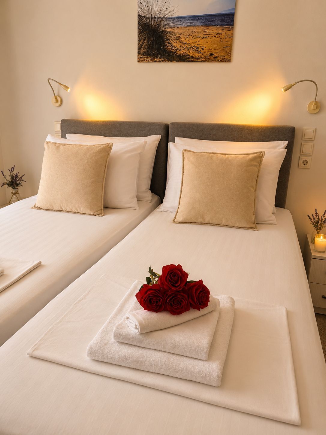 A double bed with white linens, two beige pillows, a bedside table with a candle, and a wall-mounted picture.