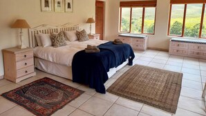 A bedroom with a bed, bedside tables, a nightstand, a window with a view, and a rug. - Barton Plover Villa near Hermanus - Pool & Hot Tub (Bot River)