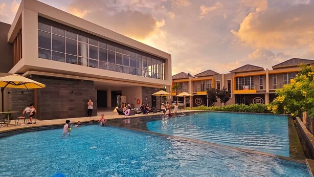 Un hotel moderno con una piscina grande, mobiliario exterior y una vista despejada del cielo.