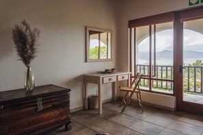 Ein Zimmer mit einem Holzkoffer, einem Schreibtisch mit Schubladen, einem Stuhl, einem Spiegel und einem großen Fenster mit Blick.