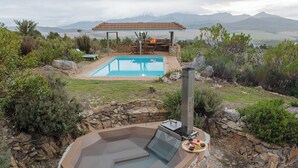 A hot tub with a stone wall, a pool, and a covered seating area with a fire feature. - Barton Hammerkop Villa nr Hermanus - HotTub & Pool (Bot River)