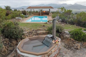 Ein Whirlpool mit Steinwand, ein Schwimmbecken und ein überdachter Sitzbereich mit Feuerstelle.