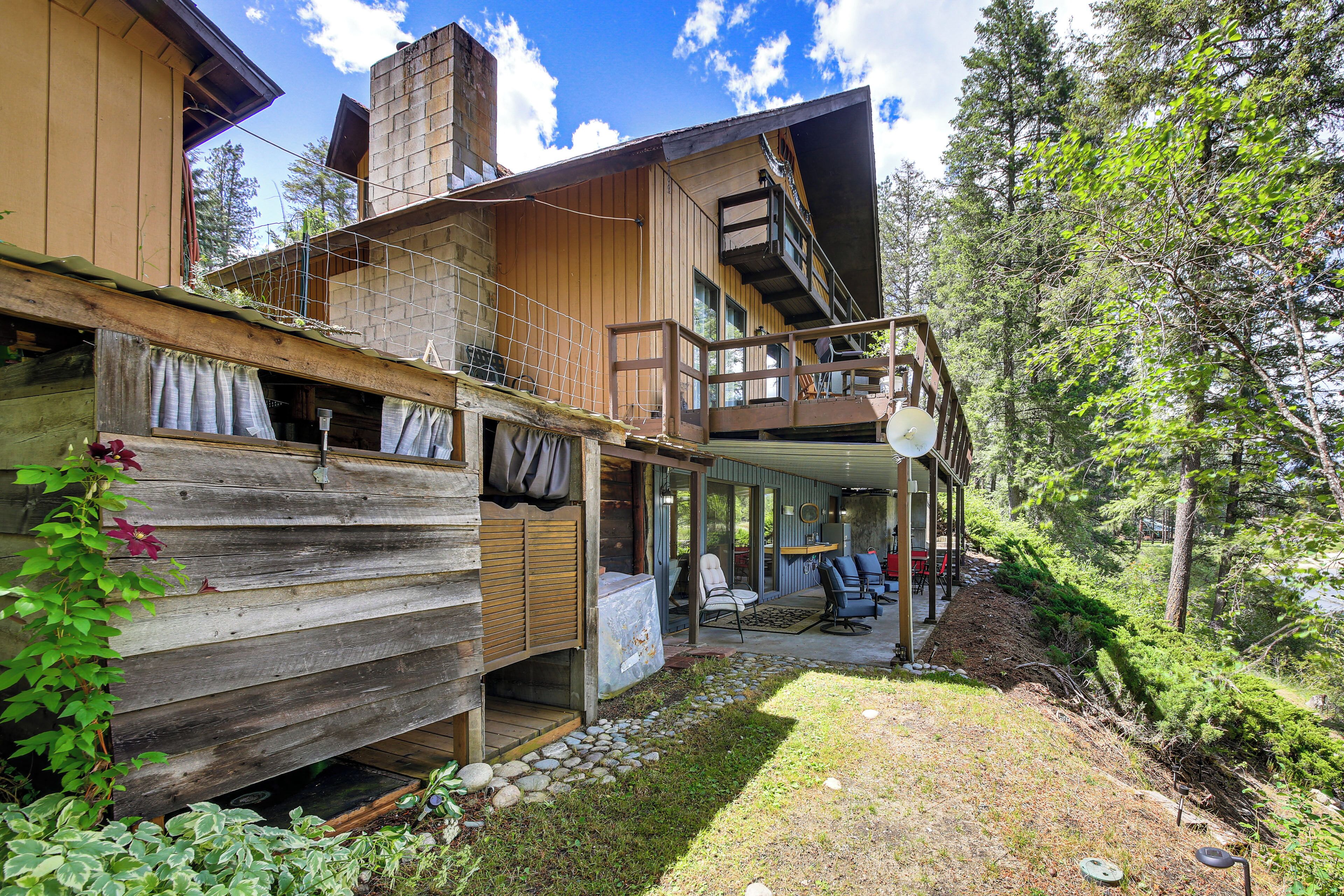 A wooden cabin with a balcony, a covered patio, and a view of the surrounding forest.