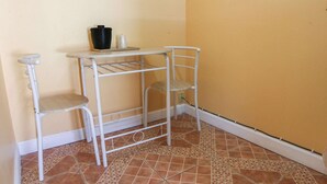 A corner room with a white metal shelf unit, two white chairs, and a tiled floor.