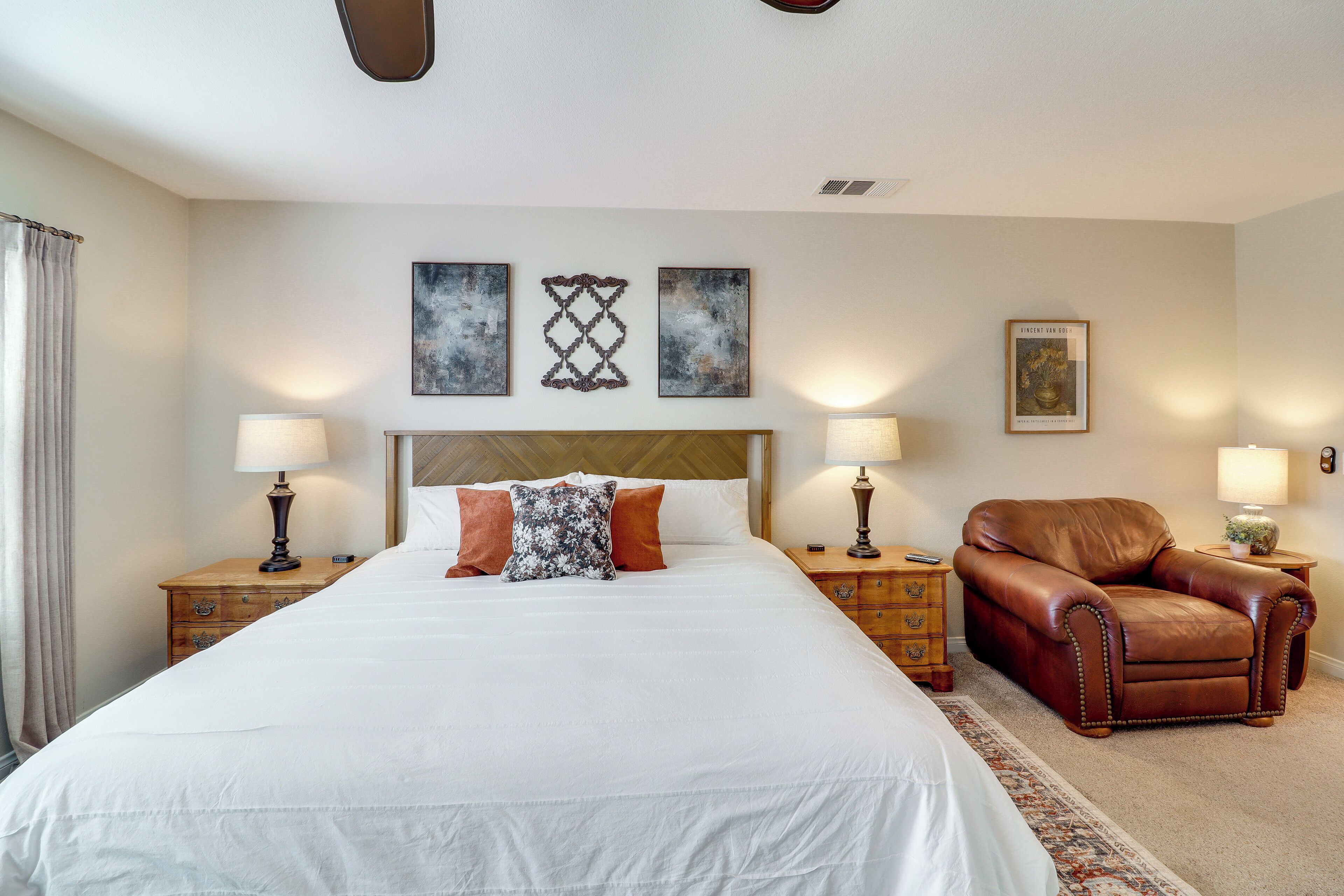 A hotel room with a large bed, two bedside tables, a brown leather armchair, and a headboard.