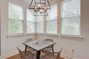 Un espace repas comprenant une table et des chaises, de grandes fenêtres équipées de stores et un luminaire suspendu.