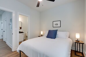 Une chambre à coucher comprenant un lit, des tables de chevet, une commode, un miroir, une porte et un couloir.