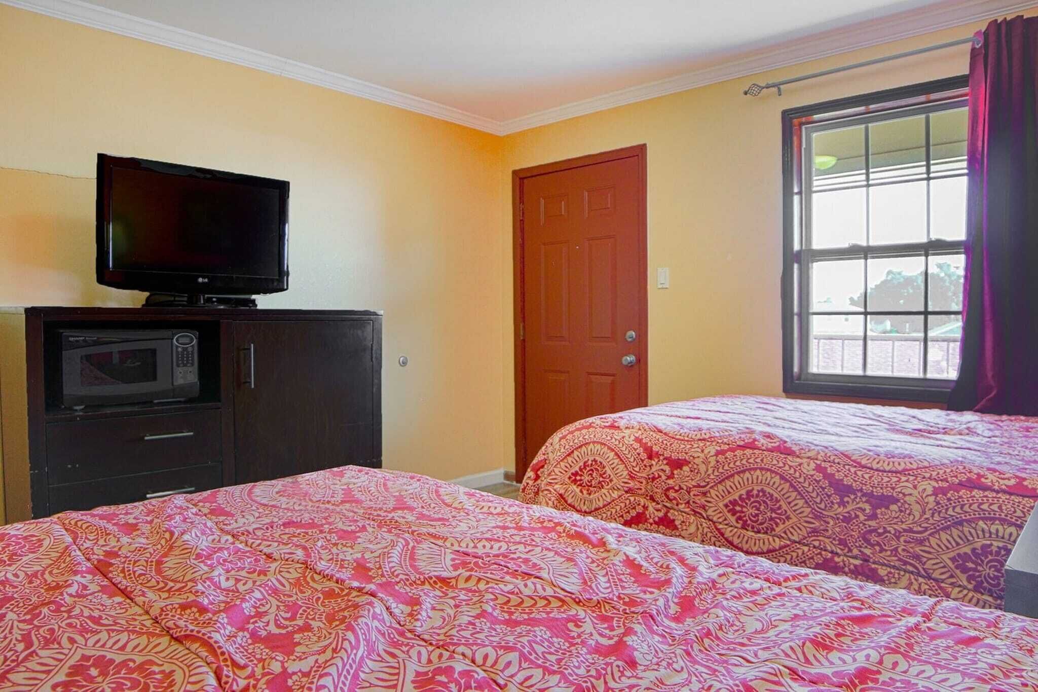 A room with two beds, a television on a cabinet, a door, and a window.