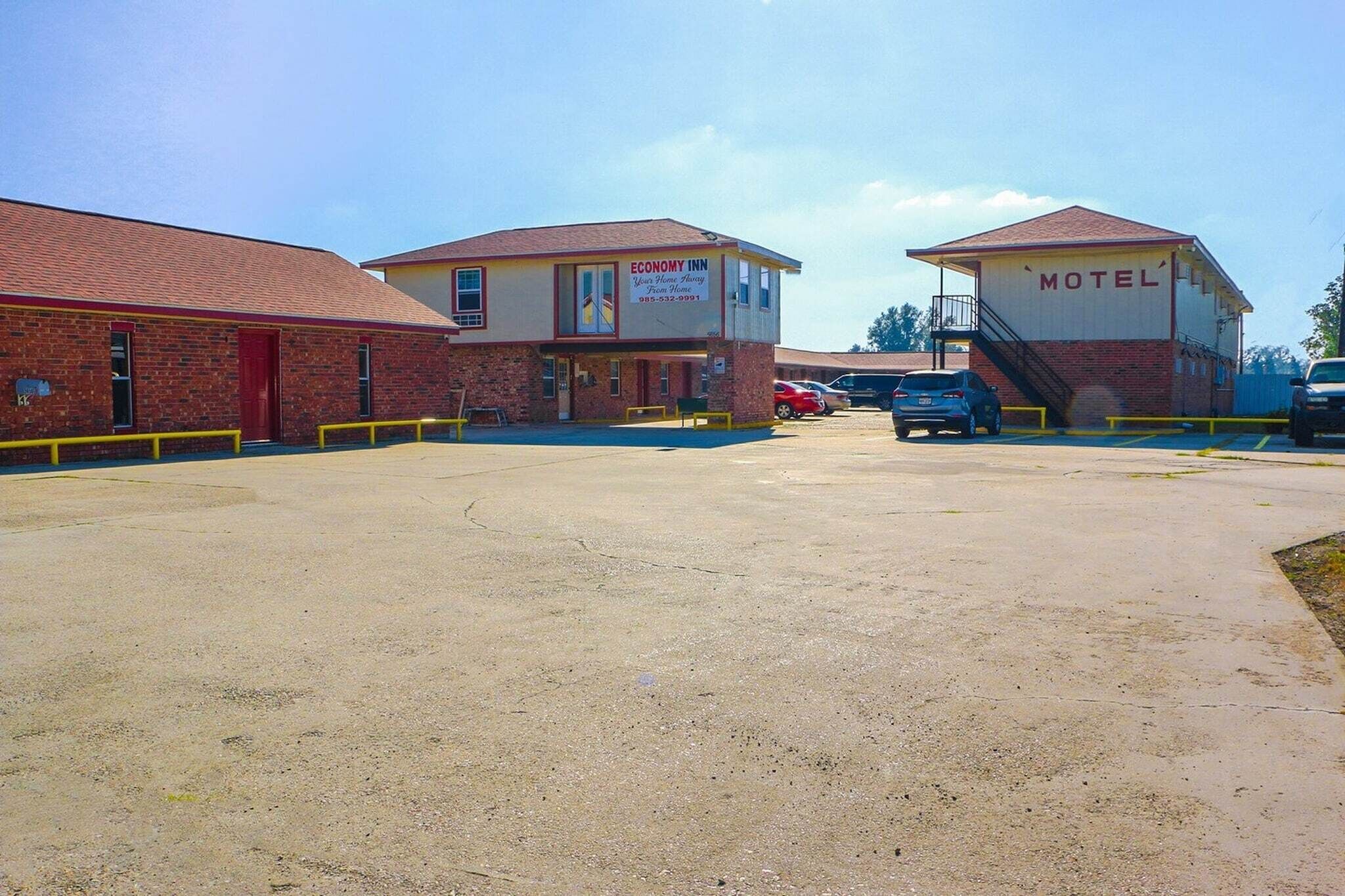 Un motel con fachada de ladrillo rojo, un letrero y un estacionamiento con coches.