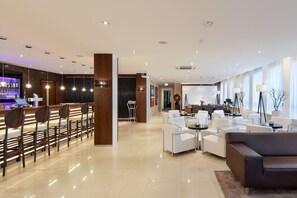 Eine moderne Hotelhalle mit Barbereich, Sitzgelegenheiten und einer Rezeption.