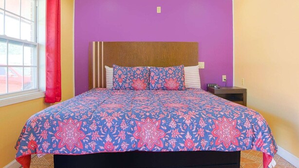 Un lit avec une couvre-lit à motifs, une tête de lit en bois et une table de chevet avec une lampe.