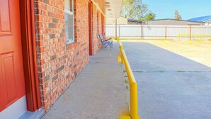 Un bâtiment en briques avec une porte rouge, un espace extérieur abrité et une barrière de sécurité jaune.