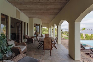 Une terrasse extérieure couverte, aménagée avec des meubles en osier, une piscine et une vue sur le paysage.