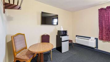 Habitación de hotel con una mesa de comedor, dos sillas, microondas, refrigerador, televisor de pantalla plana, ventana con cortinas y aire acondicionado instalado en la pared.
