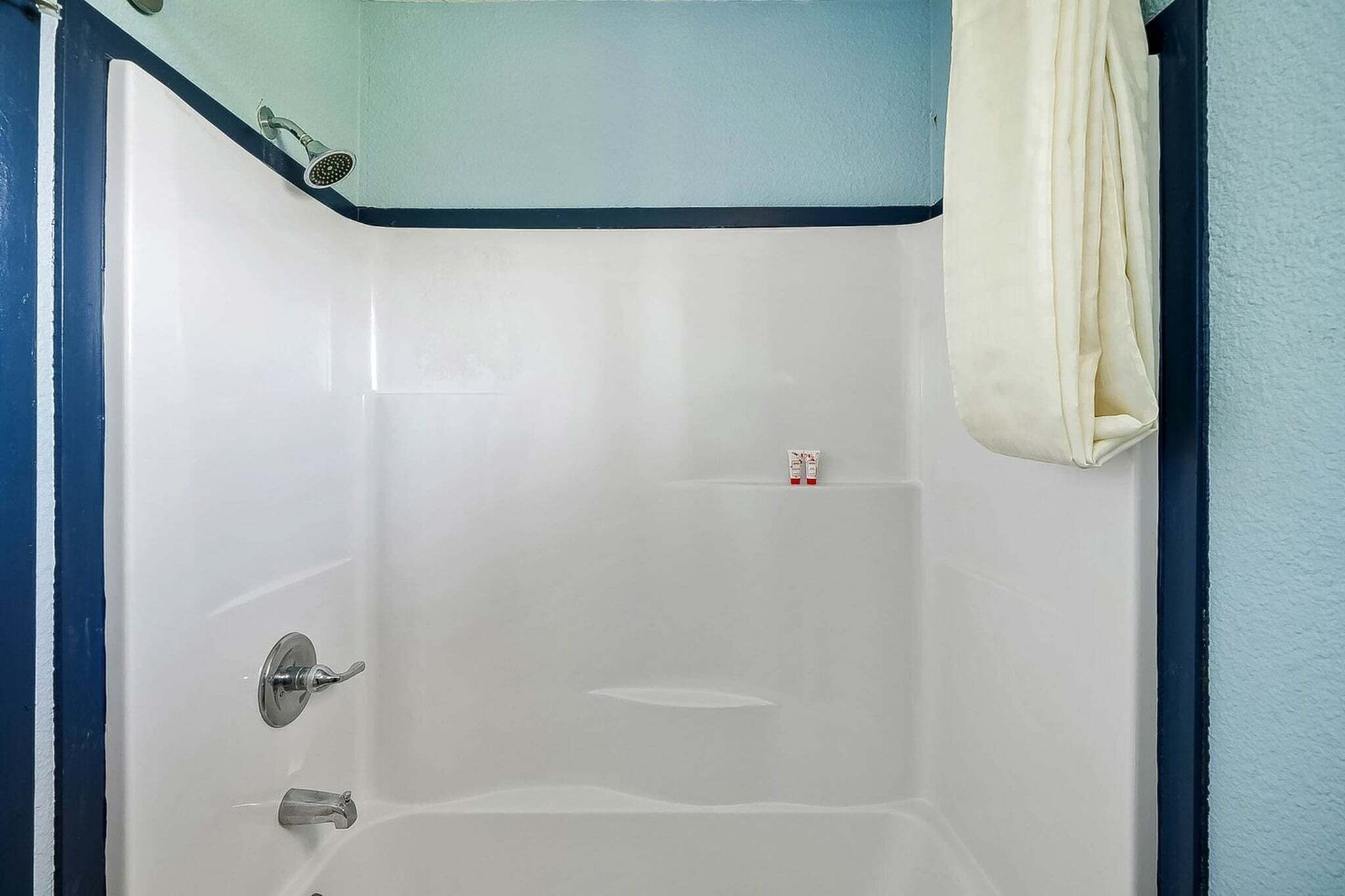 Une baignoire blanche avec un pommeau de douche, une serviette et un petit flacon de shampoing.