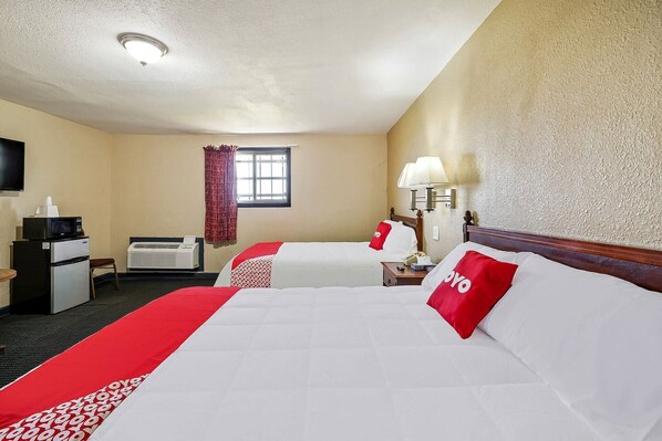 Una habitación de hotel con dos camas, un escritorio con microondas, un televisor y una ventana con cortinas.