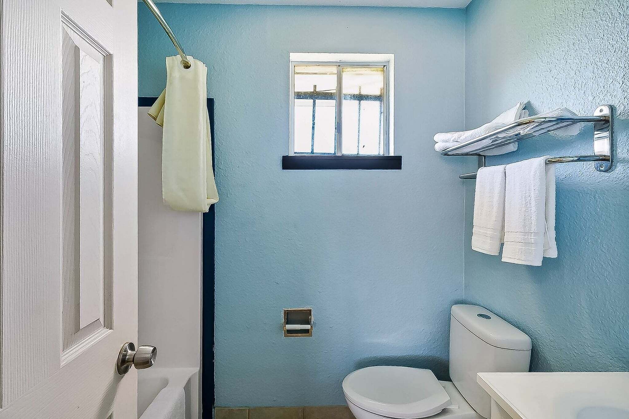 A bathroom with a toilet, a sink, a window, and a towel rack.