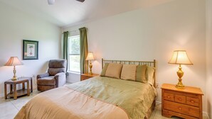 Ein Schlafzimmer mit einem Bett, einem Sessel, zwei Nachttischen, einem Deckenventilator und einem Fenster mit Vorhängen.