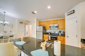 Eine moderne Küche mit Granit Arbeitsplatten, Holzschränken, Edelstahlgeräten und einem Essbereich mit weißen Stühlen und einem Tisch.