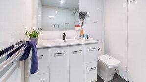 A modern bathroom with a white vanity, a mirror, a hairdryer, and a toilet.