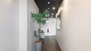 A hallway with a potted plant, a fire extinguisher, and a door with a sign.