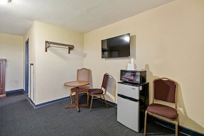 A compact hotel room with a small kitchenette, a television mounted on the wall, a single chair, and a table.