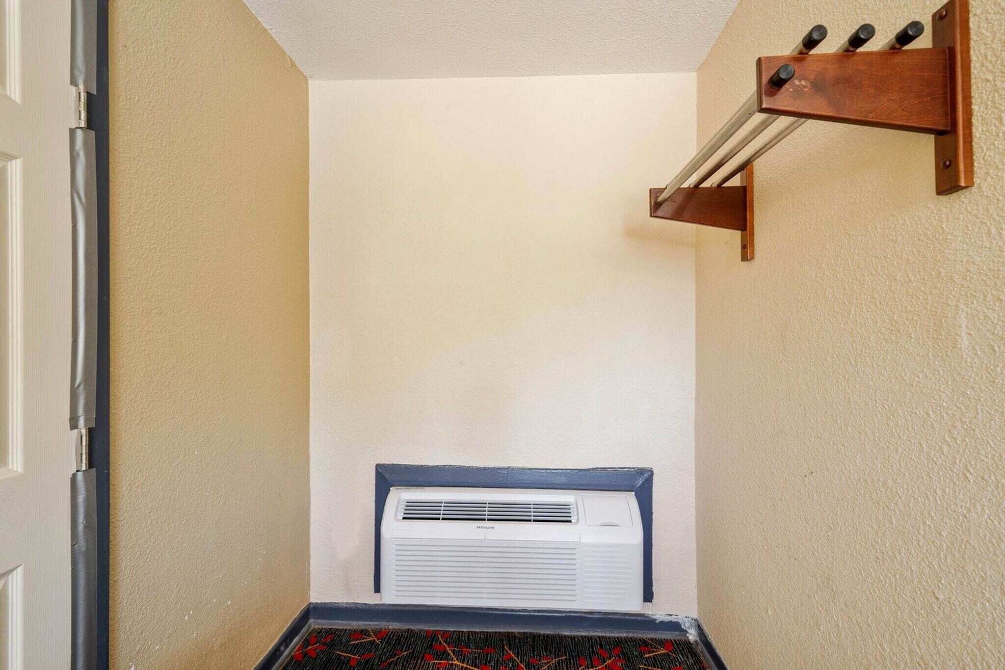 A hallway with a white air conditioning unit, a wooden rack with bottles, and a door on the left.