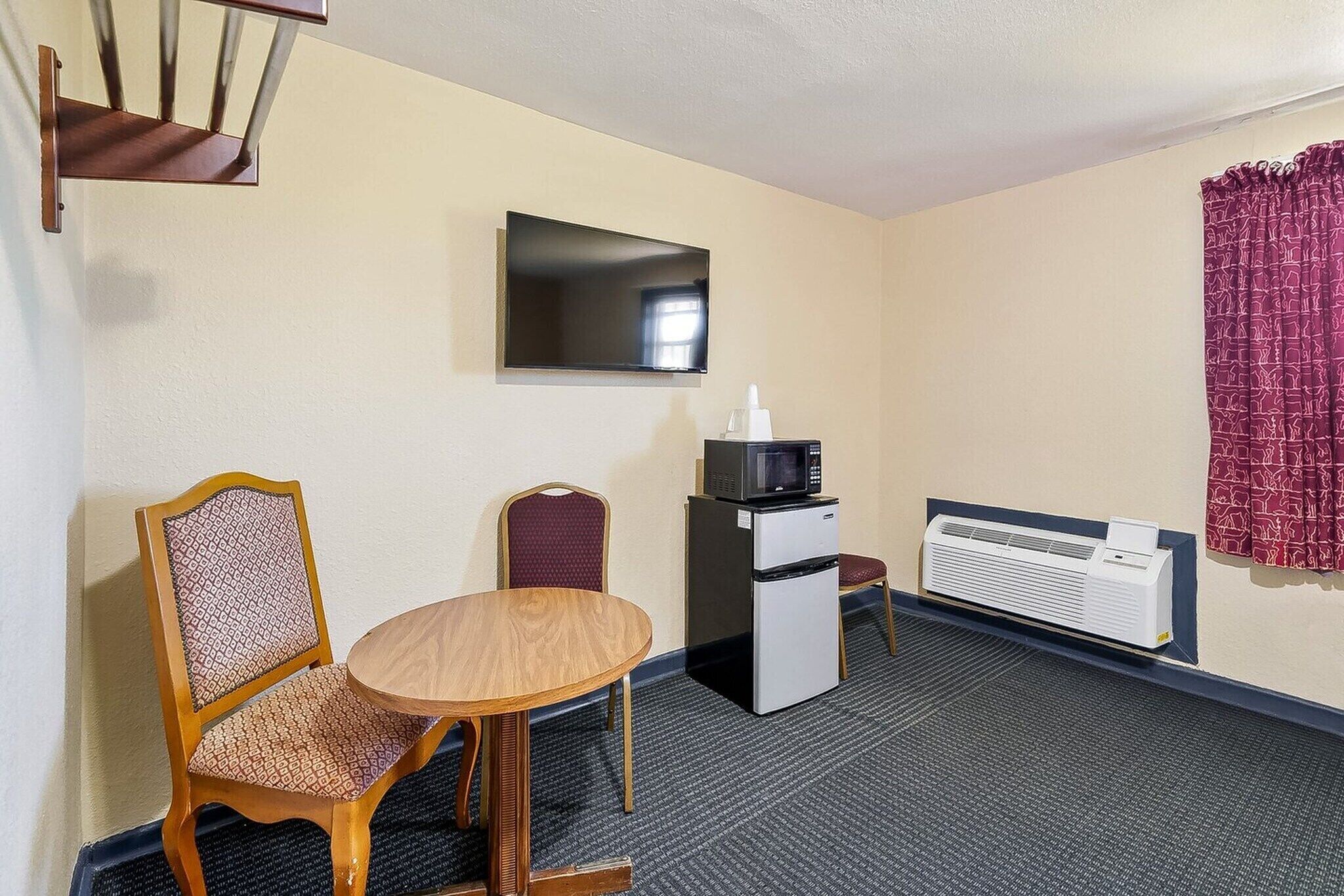 Habitación de hotel con una mesa de comedor, dos sillas, microondas, refrigerador, televisor y aire acondicionado instalado en la pared.