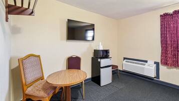 Habitación de hotel con una mesa de comedor, dos sillas, microondas, refrigerador, televisor y aire acondicionado instalado en la pared.