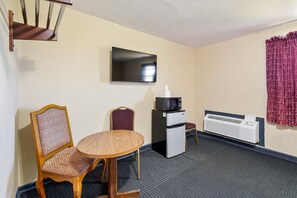 A hotel room with a dining table, two chairs, a microwave, a refrigerator, a TV, and a wall-mounted air conditioner. - Queen Bed Non-Smoking (Lockhart TX)