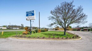Een bord van Luling Inn, een parkeerplaats en een aangelegde omgeving met een boom en struiken.