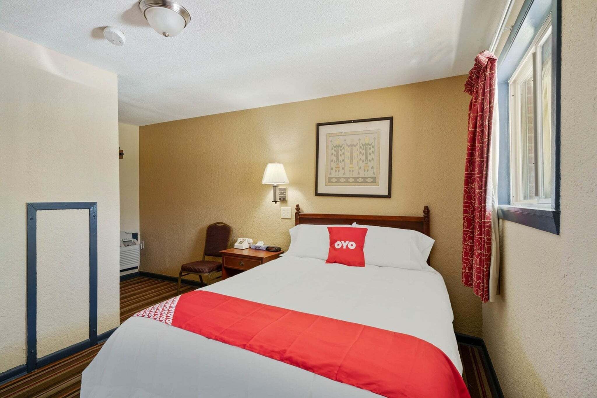A hotel room with a bed, a nightstand, a chair, a lamp, and a window with curtains.
