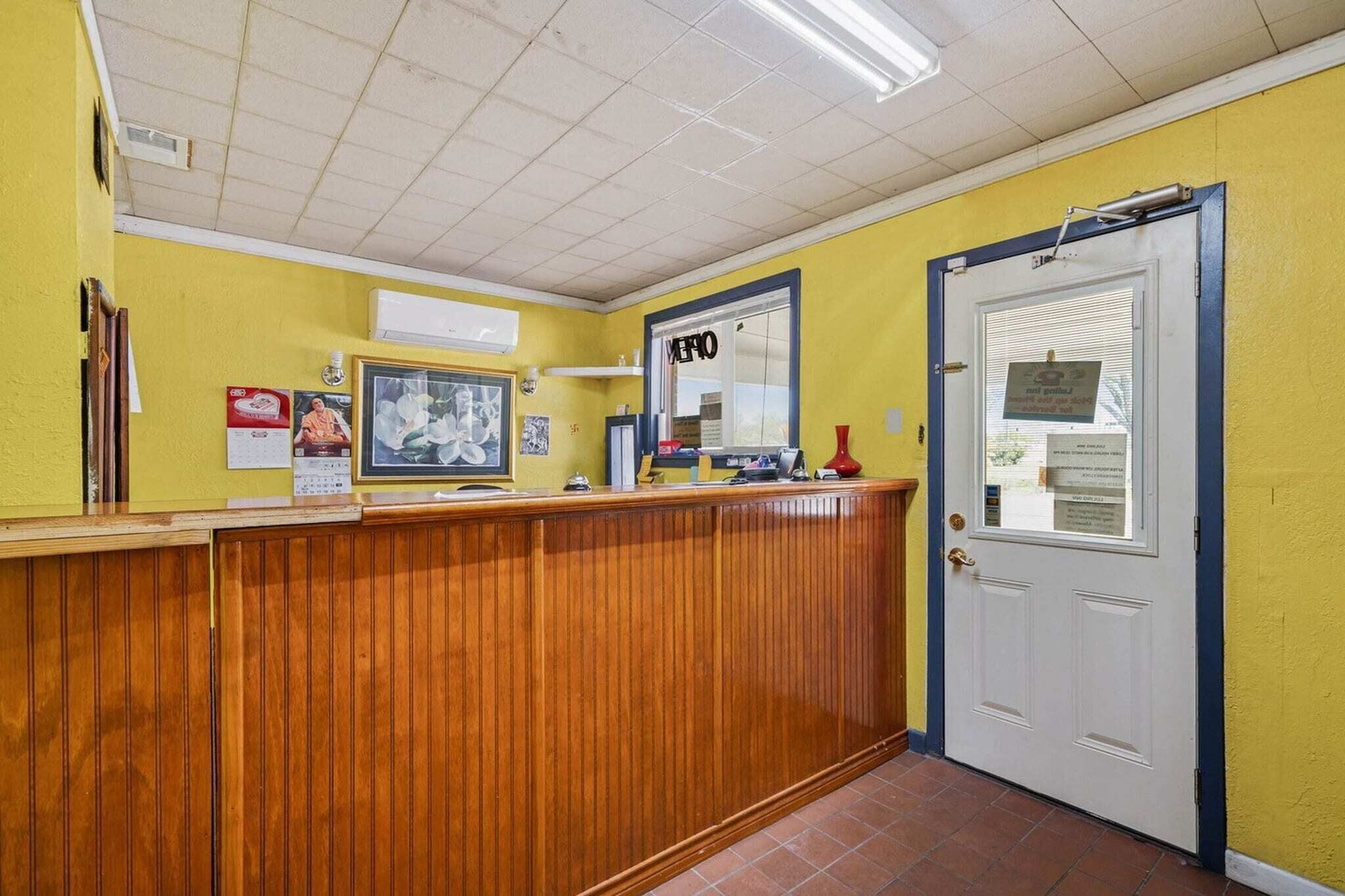 A reception area with a wooden counter, a door, and a bulletin board with notices.