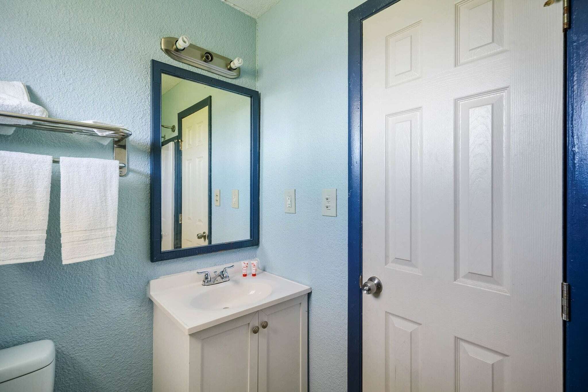 Een badkamer met een witte wastafel, een spiegel en een deur.