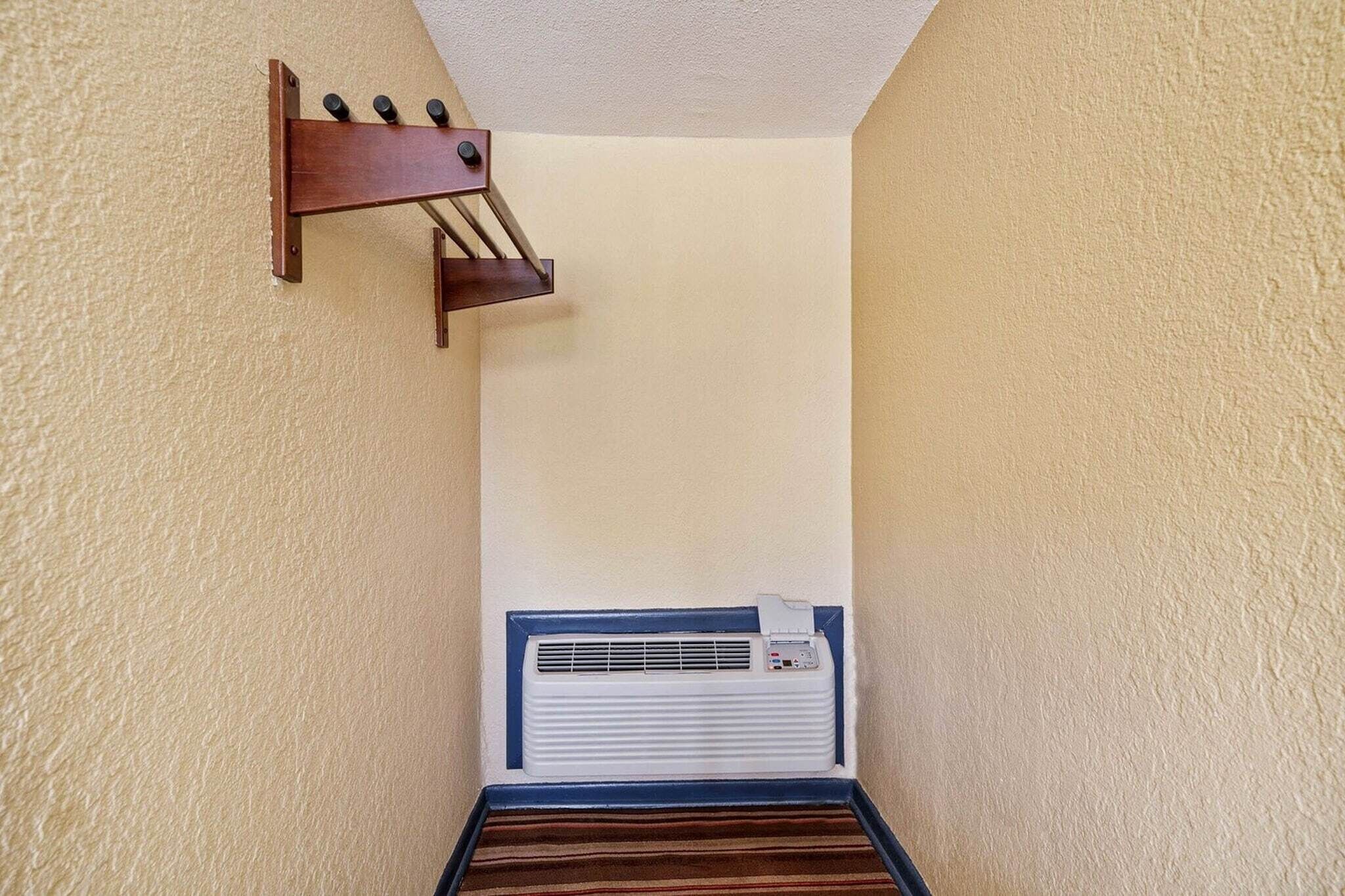 A narrow hallway with a wall-mounted air conditioning unit and a wooden rack with hooks.