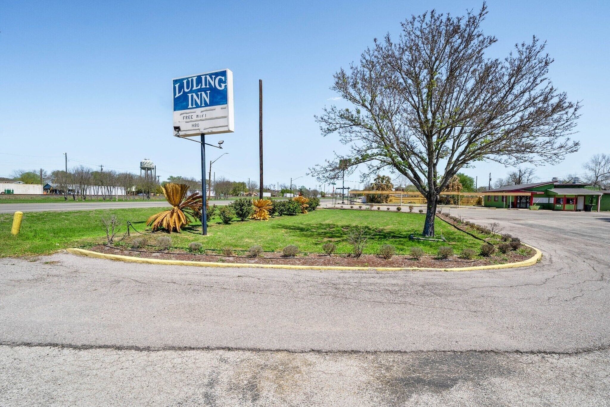 A Luling Inn sign, a parking lot, and a landscaped area with a tree and shrubs.