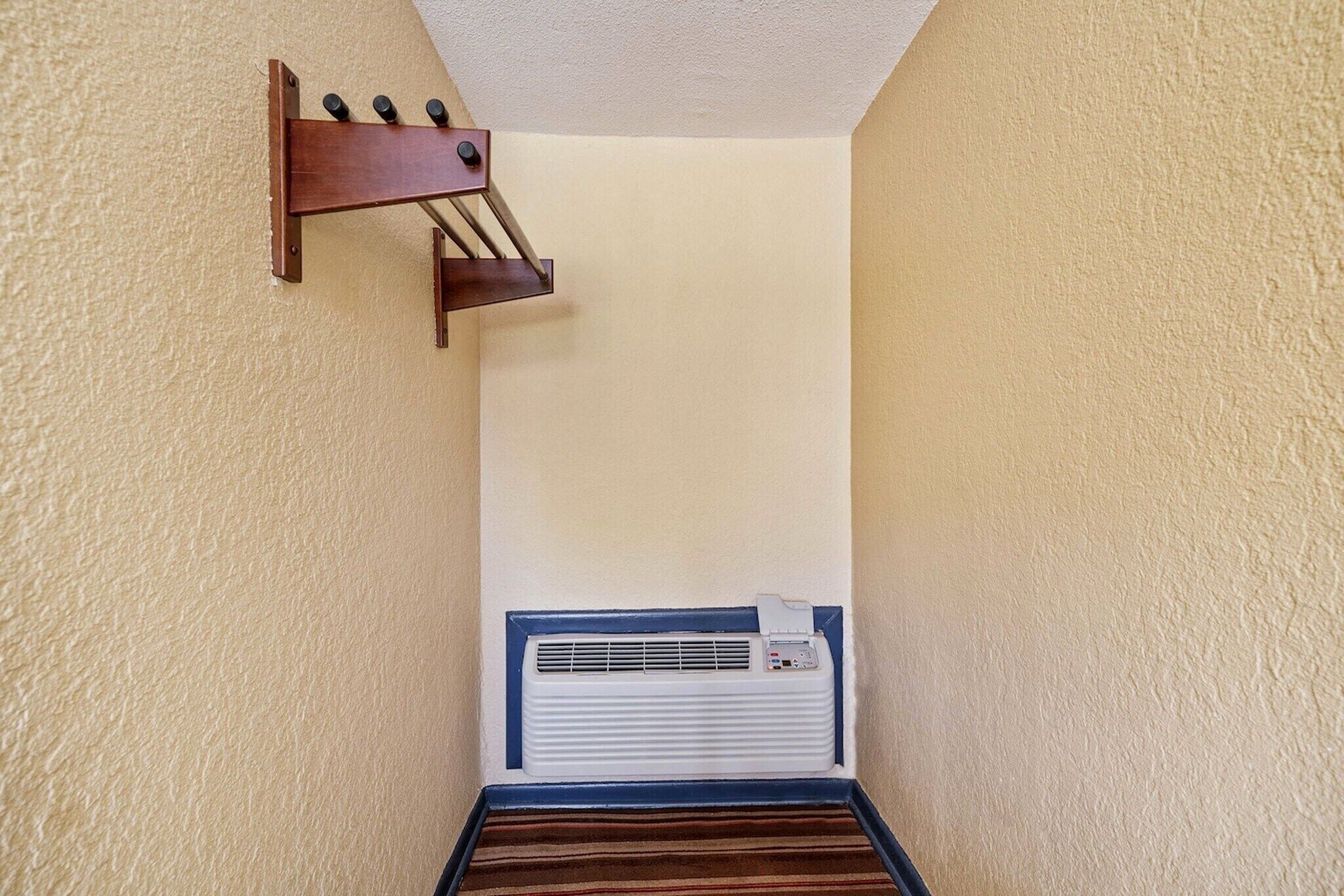 A narrow hallway with a wall-mounted air conditioning unit and a wooden rack with bottles.