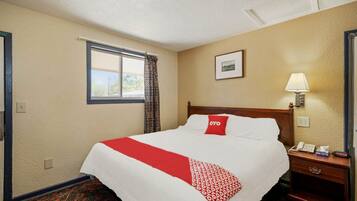 Habitación de hotel con cama, mesita de noche con lámpara, teléfono y ventana con cortinas.