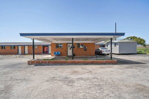 Una estación de servicio con toldo cubierto, un edificio de ladrillo y una estructura pequeña adyacente.