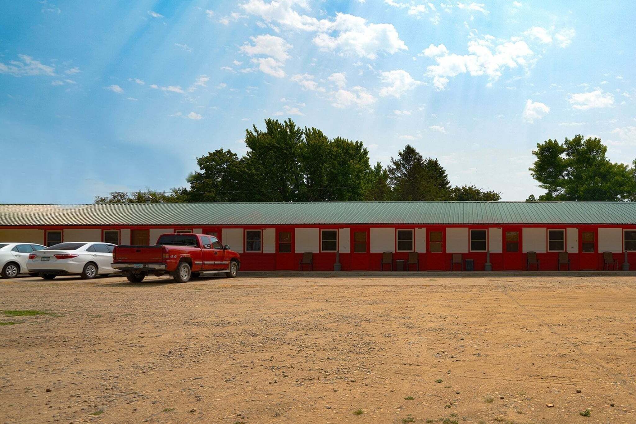 A motel with a row of rooms, a gravel parking area, and a red pickup truck parked in front.