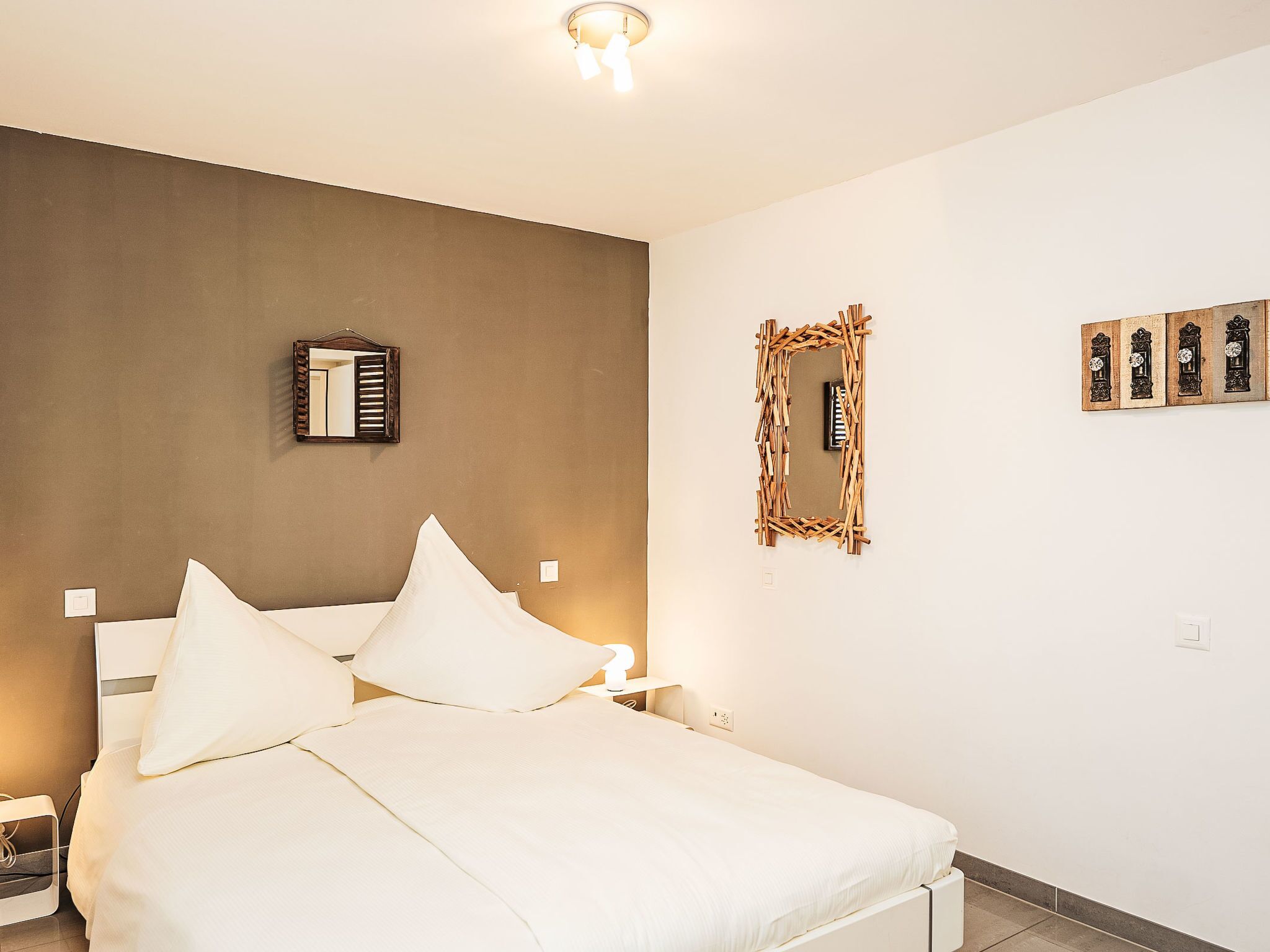 A bedroom with a bed, bedside tables, a mirror, and wall-mounted clocks.