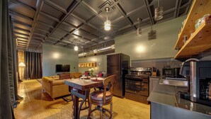 Eine moderne Küche mit Edelstahlgeräten, ein Essbereich mit Holztisch und -stühlen sowie ein gemütlicher Wohnbereich mit Sofa und Fernseher.
