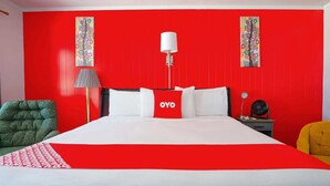 A hotel room with a red and white color scheme, a bed with white and red bedding, two wall-mounted lamps, a bedside table with a lamp, and a chair.