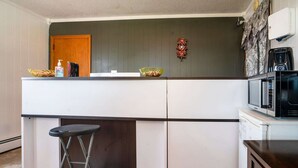A kitchen with a white countertop, a microwave, a coffee maker, and a wooden door.